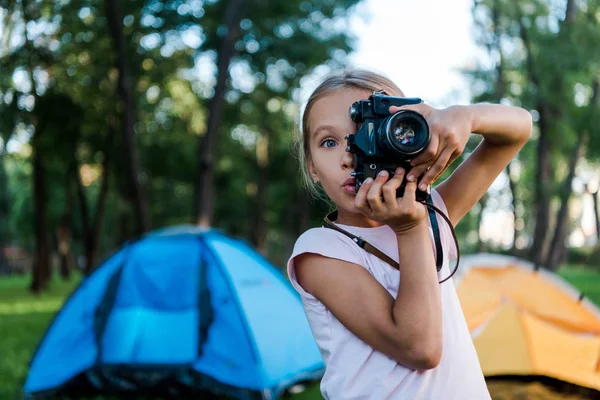 Niño sorprendido sosteniendo la cámara digital mientras toma fotos cerca de los campamentos - foto de stock