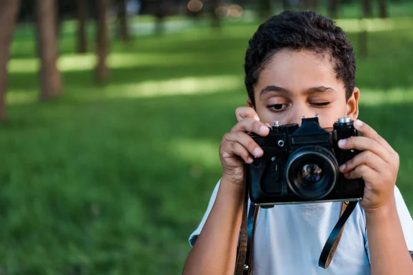 Afro-américain garçon tenant appareil photo numérique tout en parlant photo dans le parc — Photo de stock