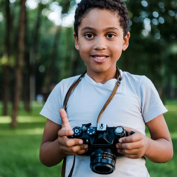 Adorable afro-américain garçon tenant appareil photo numérique dans le parc — Photo de stock
