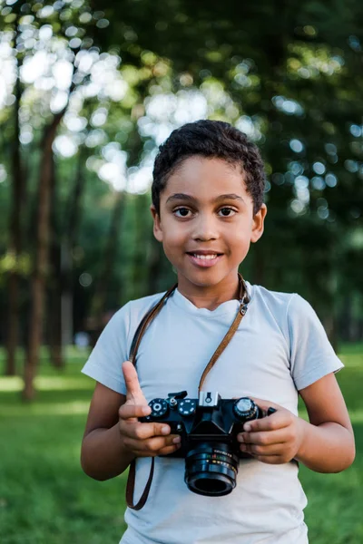 Joyeux garçon afro-américain tenant appareil photo numérique dans le parc — Photo de stock