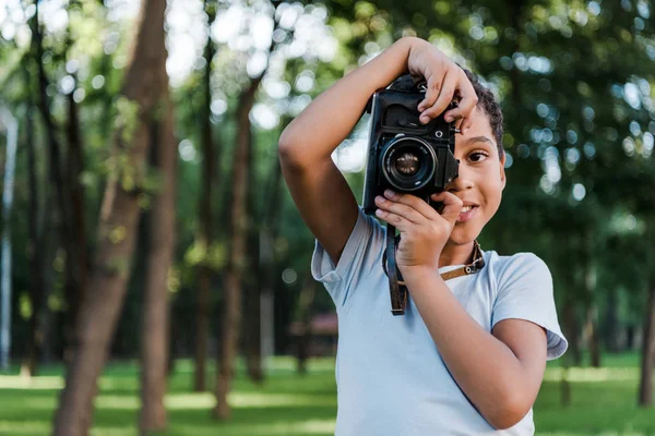 Mignon afro-américain garçon tenant appareil photo numérique tout en prenant des photos dans le parc — Photo de stock