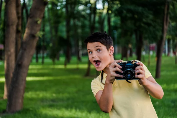 Surprised boy holding digital camera in green park — Stock Photo