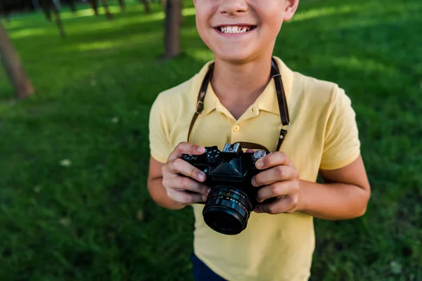 Vue recadrée de garçon heureux tenant appareil photo numérique dans le parc vert — Photo de stock
