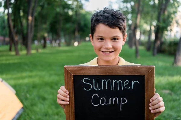 Happy boy holding chalk board with summer camp letters — Stock Photo