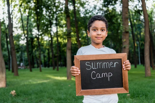 Criança americana africana feliz segurando placa de giz com letras acampamento de verão — Fotografia de Stock
