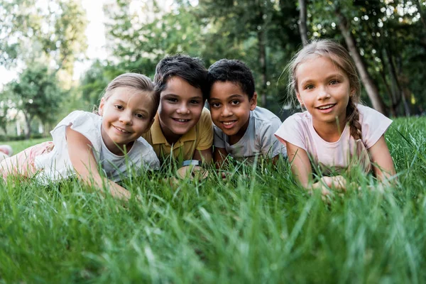 Enfoque selectivo de lindos niños multiculturales sonriendo mientras yacen en la hierba - foto de stock