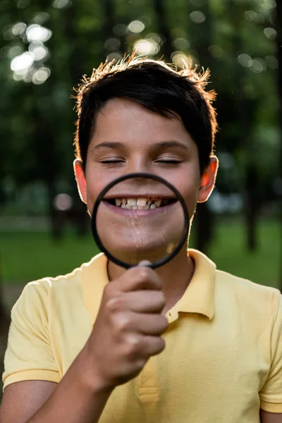 Selective focus of cheerful boy with closed eyes holding magnifier near face — Stock Photo