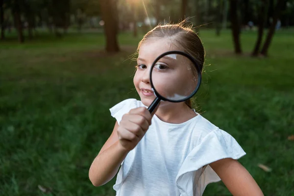 Selective focus of happy kid holding magnifier near eye — Stock Photo