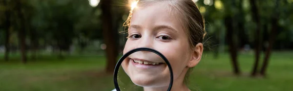 Tiro panorámico de niño feliz sosteniendo lupa cerca de la cara - foto de stock