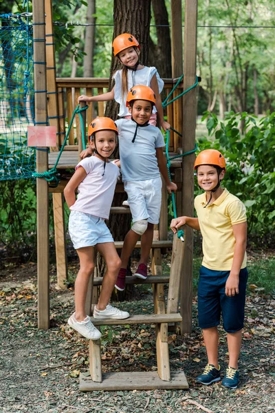 Felici bambini multiculturali in casco in piedi e sorridenti nel parco avventura — Foto stock