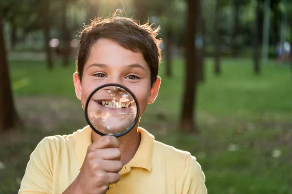 Glücklicher Junge mit Lupe in der Nähe des Gesichts beim Lächeln im Park — Stockfoto