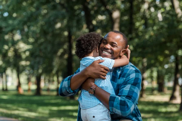 Feliz pai afro-americano com olhos fechados abraçando filho encaracolado — Fotografia de Stock