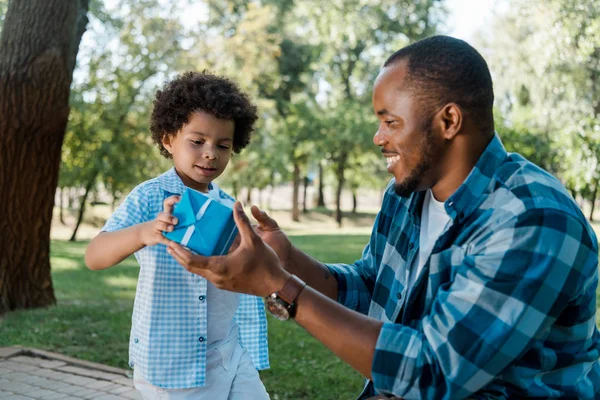 Feliz de afroamericano padre e hijo sosteniendo caja de regalo azul - foto de stock