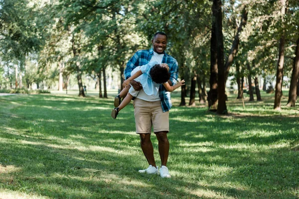 Alegre afro-americano pai segurando em braços bonito filho no parque — Fotografia de Stock