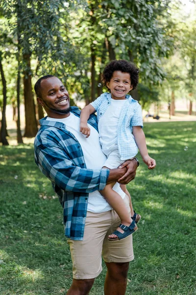 Feliz afro-americano homem segurando em braços bonito encaracolado garoto — Fotografia de Stock