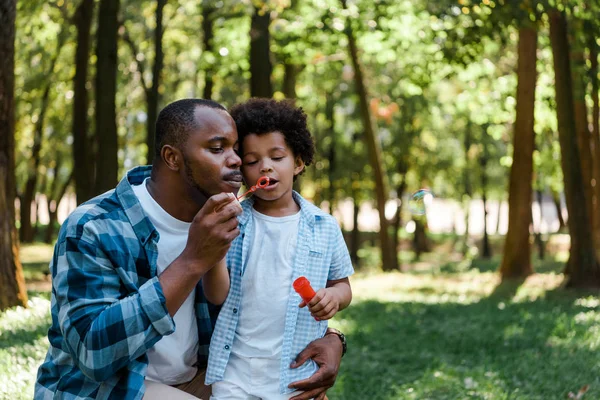 Beau père afro-américain et mignon fils soufflant bulle de savon — Photo de stock
