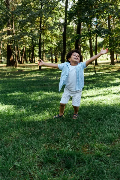 Niño afroamericano feliz con las manos extendidas en el parque - foto de stock