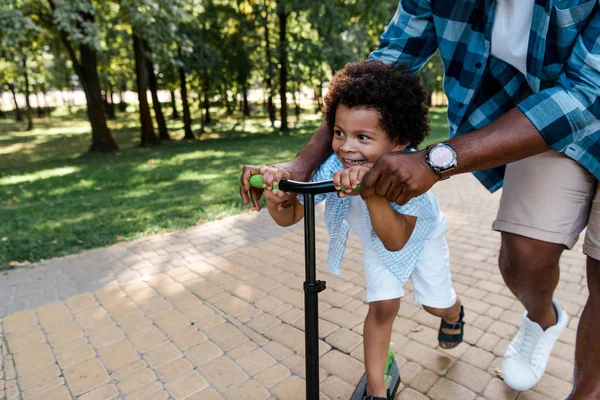 Vue recadrée du père afro-américain près fils heureux sur scooter — Photo de stock