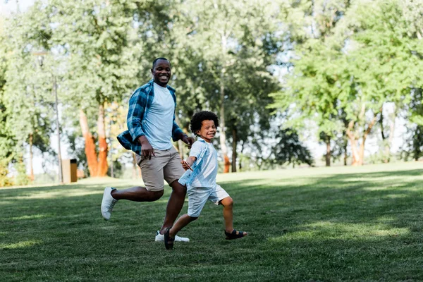 Felice padre africano americano e figlio in esecuzione su erba — Foto stock