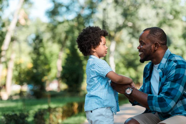 Vue latérale du père afro-américain joyeux tenant la main avec son fils — Photo de stock