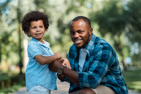 Bonito encaracolado afro-americano garoto de mãos dadas com alegre pai — Fotografia de Stock