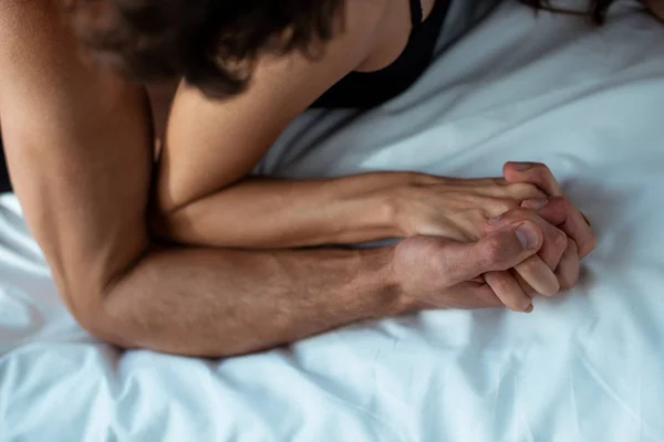 Vista ritagliata di uomo e donna appassionati che si tengono per mano in camera da letto — Foto stock