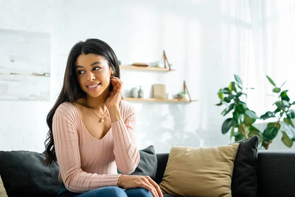 Mujer afroamericana sonriente sentada en un sofá y mirando hacia otro lado - foto de stock