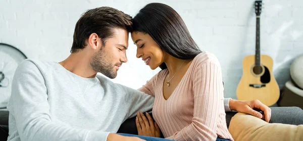 Plano panorámico de mujer afroamericana y hombre guapo con los ojos cerrados sonriendo y abrazándose en apartamento - foto de stock