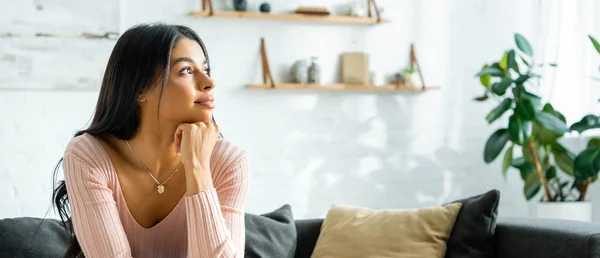 Panoramic shot of pensive african american woman sitting on sofa and looking away — Stock Photo