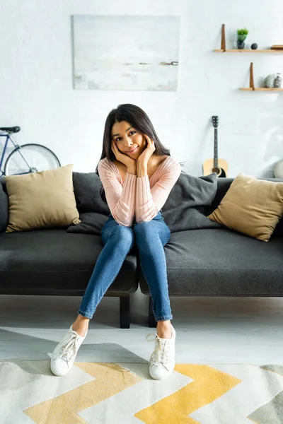 Mujer afroamericana sonriente sentada en el sofá y mirando a la cámara - foto de stock