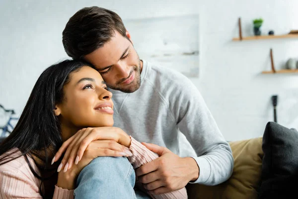 Africano americano mujer y guapo hombre sonriendo y abrazando en apartamento - foto de stock