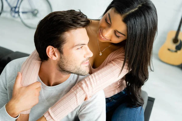 Africano americano mujer y guapo hombre sonriendo y abrazando en apartamento - foto de stock