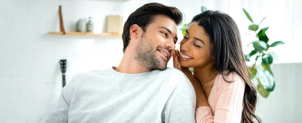 Panoramic shot of african american woman and handsome man smiling and looking at each other in apartment — Stock Photo