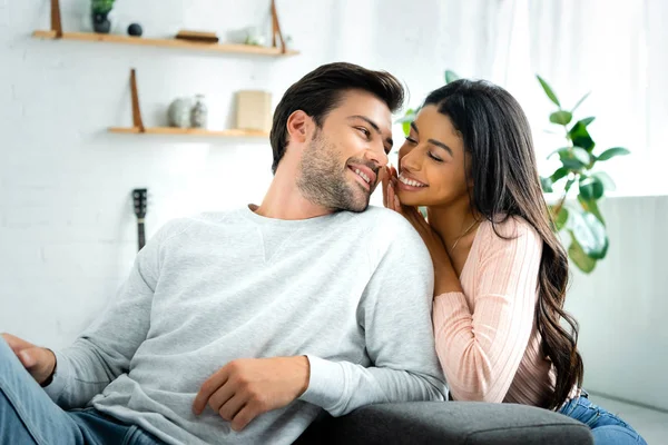 Mujer afroamericana y hombre guapo sonriendo y mirándose en el apartamento - foto de stock