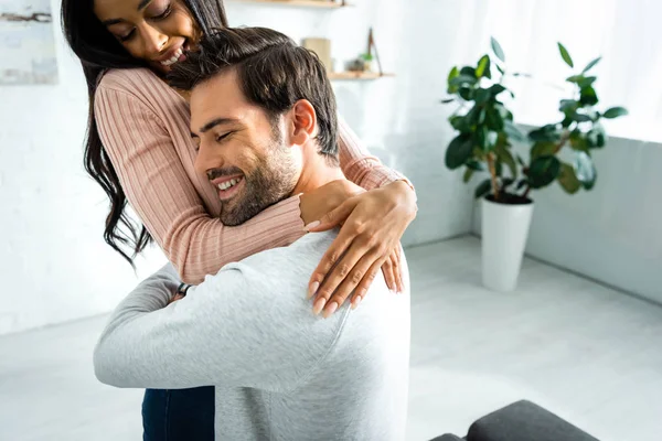 Afroamerikanerin und schöner Mann lächeln und umarmen sich in Wohnung — Stockfoto