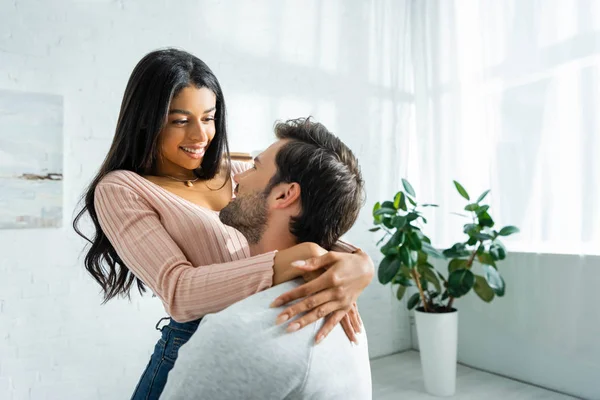 Africano americano mujer y guapo hombre sonriendo y abrazando en apartamento - foto de stock