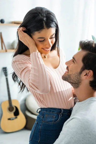 Afroamerikanerin und schöner Mann lächeln und umarmen sich in Wohnung — Stockfoto