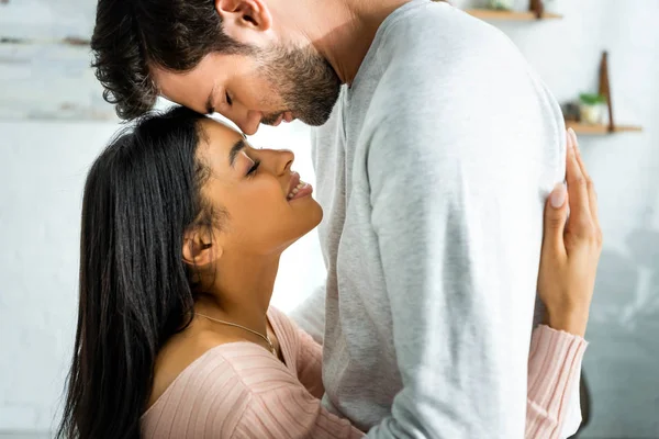 Side view of african american woman and handsome man smiling and hugging in apartment — Stock Photo