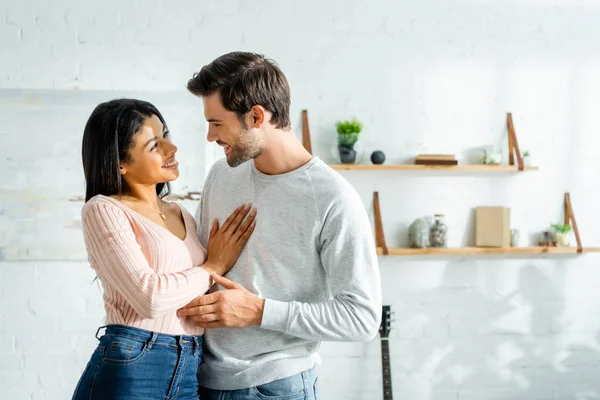 Afroamerikanerin und schöner Mann lächeln und umarmen sich in Wohnung — Stockfoto