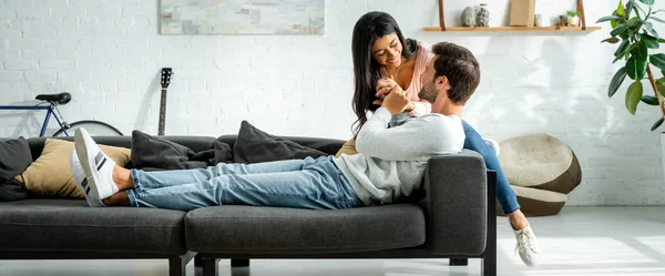 Panoramic shot of african american woman and handsome man smiling and hugging in apartment — Stock Photo