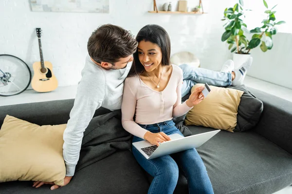 African american woman with laptop holding credit card and looking at man — Stock Photo