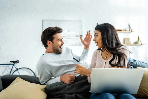 Sorprendió a la mujer afroamericana con el ordenador portátil con tarjeta de crédito y mirando al hombre - foto de stock