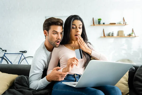 Chocado Africano americano mulher segurando cartão de crédito e olhando para laptop com o homem — Fotografia de Stock