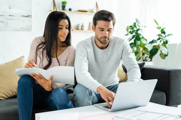 Afrikanische Amerikanerin erledigt Papierkram und schöner Mann benutzt Laptop in Wohnung — Stockfoto