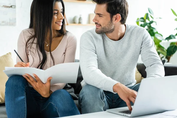African american woman doing paperwork and handsome man using laptop in apartment — Stock Photo