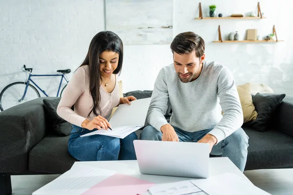 Afrikanische Amerikanerin erledigt Papierkram und schöner Mann benutzt Laptop in Wohnung — Stockfoto