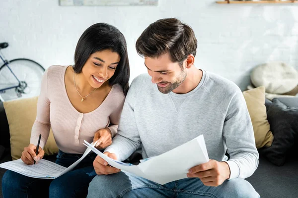 Lächelnde afrikanisch-amerikanische Frau und gutaussehender Mann, der Papierkram in der Wohnung erledigt — Stockfoto