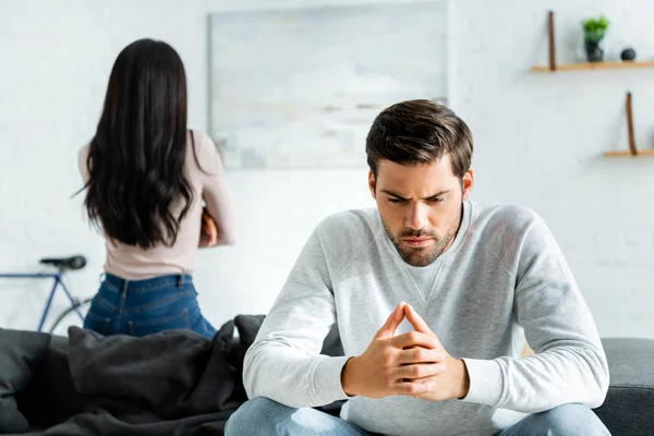 Enfoque selectivo de hombre triste y guapo y mujer afroamericana sentado en el sofá - foto de stock