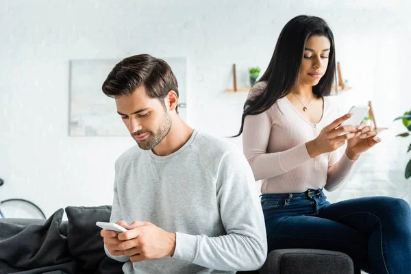 Handsome man and african american woman sitting on sofa and using smartphones — Stock Photo