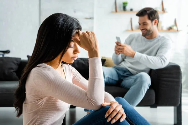 Selective focus of sad african american woman and man using smartphone — Stock Photo
